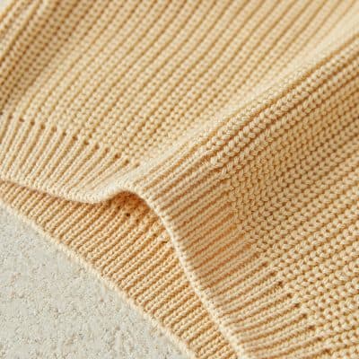 Soft beige knitted beach mat on sandy surface, perfect for outdoor relaxation and sunbathing, offering comfort and style for beachgoers.