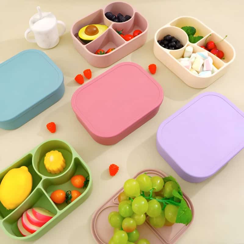 Colorful plastic bento boxes for kids with healthy snack compartments, including fruits, vegetables, and candies, on a light background for convenient meal storage and organization.