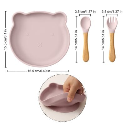 Soft pink bear-shaped silicone plate with removable divided sections, perfect for kids’ meals, and matching wooden spoon and fork, ideal for pediatric dentistry and child-friendly dining.