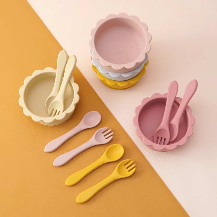 Colorful silicone children's bowls and utensils set, perfect for kids' meals and snacking, featuring soft pastel pink, yellow, and white colors.