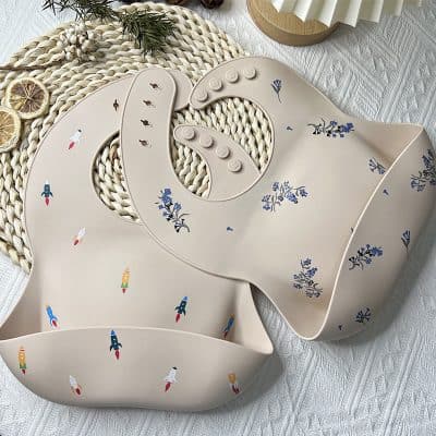 Rocket and floral-themed silicone baby bibs, stylish and practical for feeding time, easy to clean, flexible, and durable for infants' comfort and mess management.