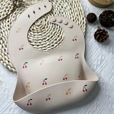 Cherry-themed baby silicone bib featuring adjustable neck straps and a food catcher, perfect for feeding time, with a cute cherry print design for infants.