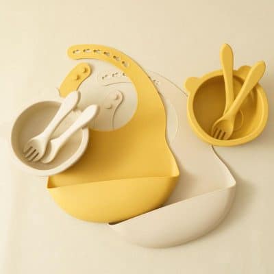 Colorful baby dining utensils set including bowls and spoons in yellow and white, designed for nursery feeding and baby care, perfect for modern parenting.