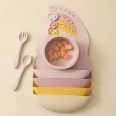 Stylish baby feeding set with matching utensils, colorful divided plates, and a bowl with snacks on pastel background for toddler mealtime.
