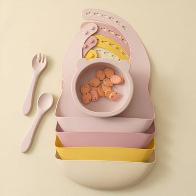 Stylish baby feeding set with matching utensils, colorful divided plates, and a bowl with snacks on pastel background for toddler mealtime.
