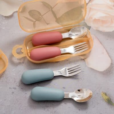 Silicone baby utensils set including pink and blue handles with stainless steel spoons and forks, stored in a travel case, ideal for kids' dining and baby food feeding.
