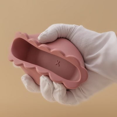 Pink scalloped-edged silicone eyelash extension remover tray held by a gloved hand for eye care and beauty treatments.