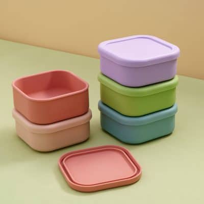 Colorful silicone storage containers in pastel shades stacked on a pastel background, ideal for food storage and organization.