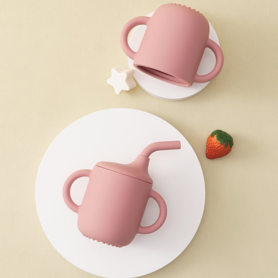 Pink sippy cups with handles on a light beige background, ideal for children’s feeding accessories and baby drinkware.