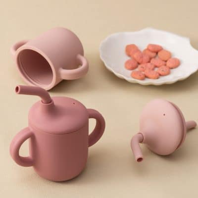 Pink silicone watering cans for children's play, with a white dish of colorful candies on a beige background.