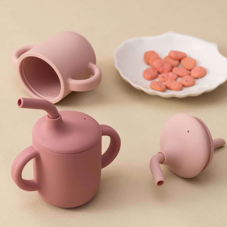 Pink silicone watering cans for children's play, with a white dish of colorful candies on a beige background.