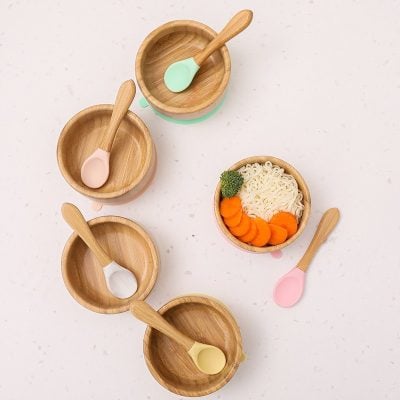 Natural wooden bowls with pastel-colored spoons, some containing baby food like noodles and vegetables, ideal for infants and young children at Monalisa Store.