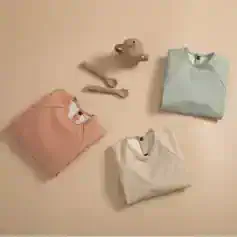 Soft pastel-colored folded shirts with clothing tags, small ceramic teapot, and bamboo utensils, displayed on a neutral background, emphasizing stylish and comfortable clothing options at Monalisa Store for optimal eye comfort and fashion.