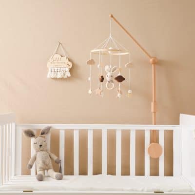 Soft beige baby nursery with a white crib, plush bunny toy, and pastel mobile featuring stars, clouds, and a bunny, creating a cozy and stylish Monalisa Store-inspired baby room decor.