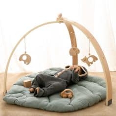 Wooden baby play gym with hanging toys on soft plush mat for infant tummy time and sensory development.
