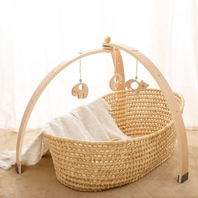 Handmade baby bassinet with wooden mobile and soft white blanket, natural woven wicker structure, ideal for nurseries and newborns, stylish and cozy for infant sleeping and comfort.