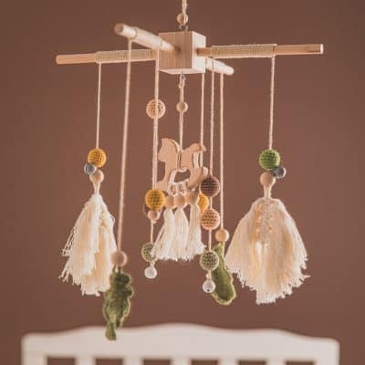 Colorful baby mobile with wooden elements, yarn balls, and a rocking horse, perfect for nursery decor and soothing infants.