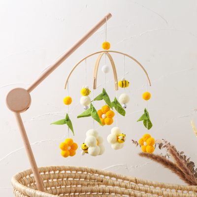 Soft baby mobile with yellow, white, and green felt floral and bee decorations, wooden arm hanging above a woven basket, nursery decor for infants and toddlers.