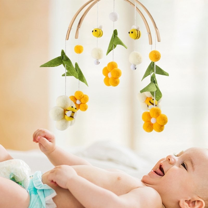 Colorful baby mobile with felt flowers, bees, and leaves hanging above a smiling baby in a crib, perfect for a nursery or baby room decor.