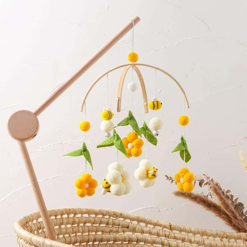 Beaded baby crib mobile with yellow, white, and green felt flowers and bumblebee accents hanging above a woven bassinet, ideal for nursery decor and sensory stimulation.