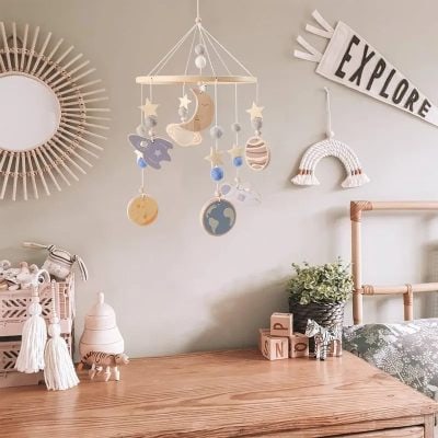 Colorful space-themed baby mobile hanging above a wooden changing table, with plush toys, blocks, and decorative accents, creating a playful nursery environment.