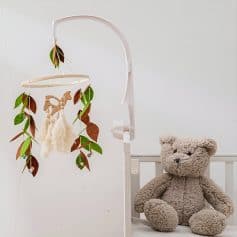 Soft toy teddy bear and baby crib with personalized baby mobile, nursery decor, and gentle lighting for a cozy infant room setting.