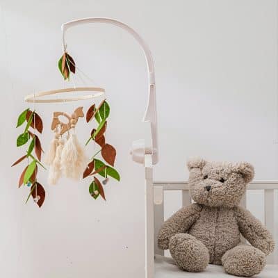 Soft toy teddy bear and baby crib with personalized baby mobile, nursery decor, and gentle lighting for a cozy infant room setting.