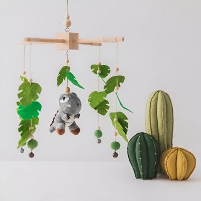Handmade felt cactus wall decor with plush dinosaur toy, tropical leaf accents, and wooden beaded details, ideal for baby room nursery or children's decor, eco-friendly and stylish.