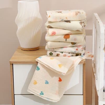 Soft baby muslin cloths with colorful heart patterns stacked on a wooden nightstand alongside a modern white vase, perfect for newborns and baby care, ideal for soothing and cleaning at Monalisa Store.