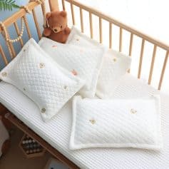 Cuddly bear plush toy nestled among soft, baby-safe bedding with adorable animal and star prints in a cozy nursery setting.