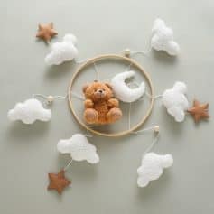 Soft plush teddy bear surrounded by fluffy cloud and star-shaped decorations, ideal for nursery or baby room décor, emphasizing adorable and cozy atmosphere for infants.