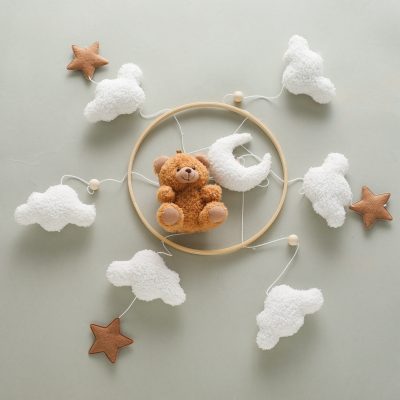 Soft plush teddy bear surrounded by fluffy cloud and star-shaped decorations, ideal for nursery or baby room décor, emphasizing adorable and cozy atmosphere for infants.