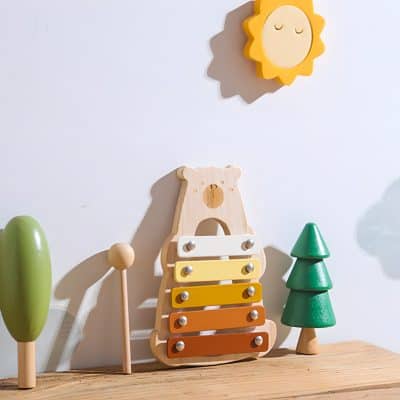 Bright wooden toy xylophone with colorful bars, set against a playful children's room decor featuring trees and sun wall art, ideal for kids' sensory and musical development.