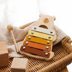 Colorful wooden xylophone for children, educational musical toy for early childhood development, placed on wicker basket with soft fabric and wooden blocks, ideal for kids' learning and play.