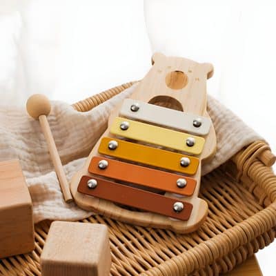 Colorful wooden xylophone for children, educational musical toy for early childhood development, placed on wicker basket with soft fabric and wooden blocks, ideal for kids' learning and play.