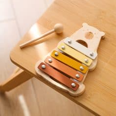 Colorful wooden xylophone with bear-shaped wooden percussion instrument on a light wooden table for children's musical education and sensory development.