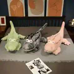 Crocodile plush toys in pastel green, gray, and pink, displayed on a bed with artwork in the background, emphasizing cute, whimsical decor and plush collection at Monalisa Store.