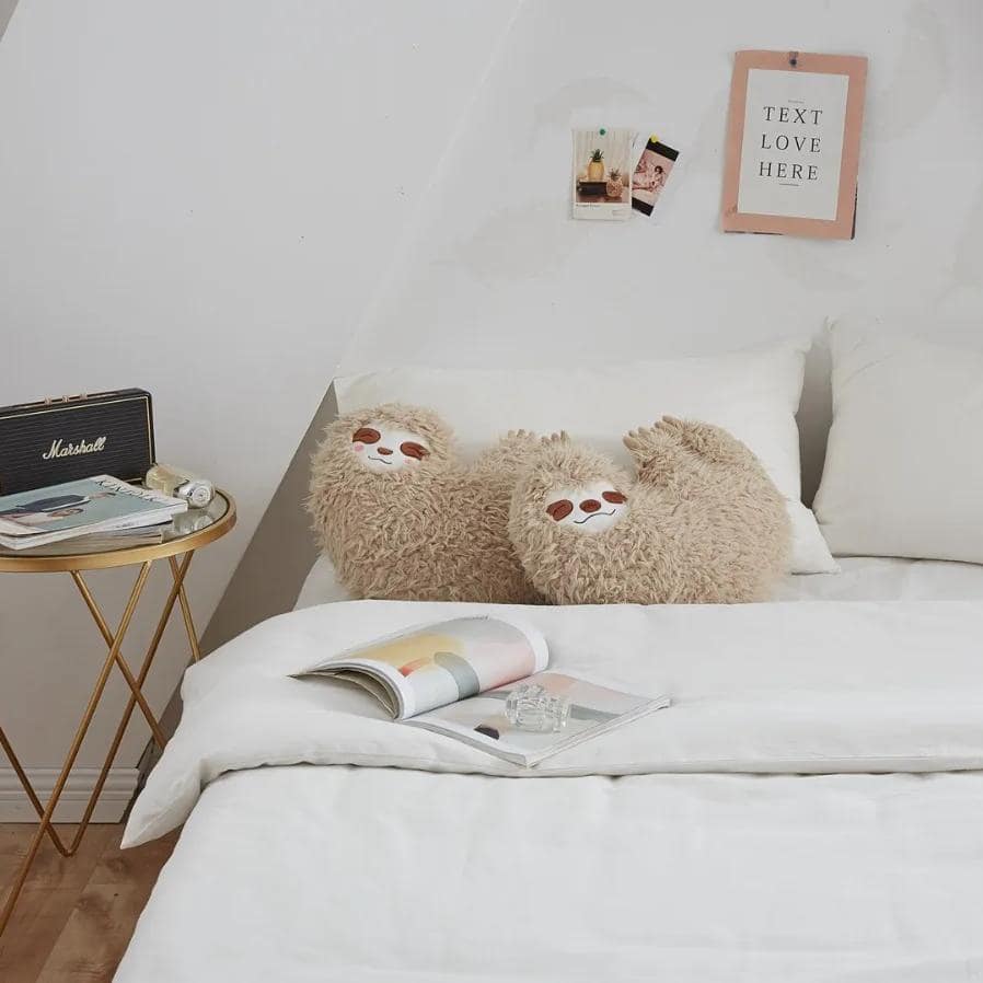 Soft plush sloth-shaped cushions on a cozy white bed, perfect for creating a relaxing atmosphere in an optometry or eyewear store's interior decor.