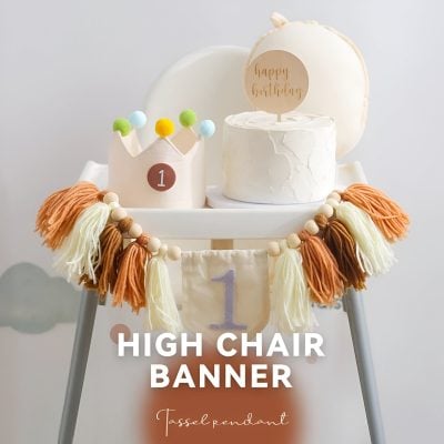 Colorful high chair birthday banner with tassel pendant, perfect for first birthday celebrations, decorated with a white cake and "happy birthday" topper, ideal for baby and kids parties.