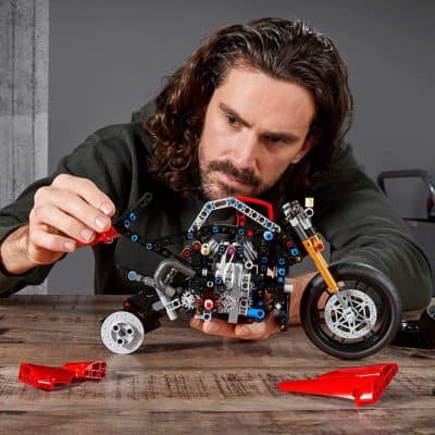Detailed image of a man assembling a LEGO motorcycle model, focusing on precision and craftsmanship, showcasing fun and creative building. Ideal for tech enthusiasts and LEGO fans.