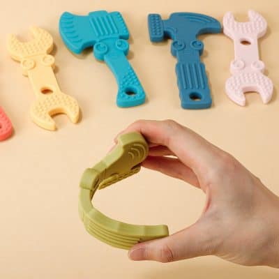 Flexible silicone baby teether in the shape of tools, including hammer and wrench, for soothing sore gums and encouraging dental development. Bright colors and ergonomic design.