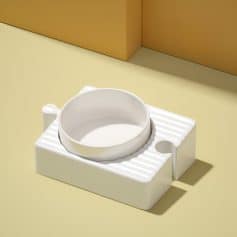White ceramic pet food bowl with textured stand on a yellow surface with beige background.