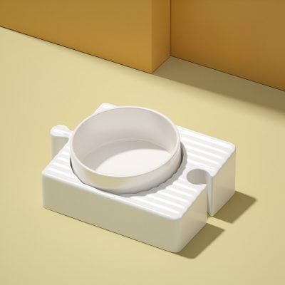 White ceramic pet food bowl with textured stand on a yellow surface with beige background.