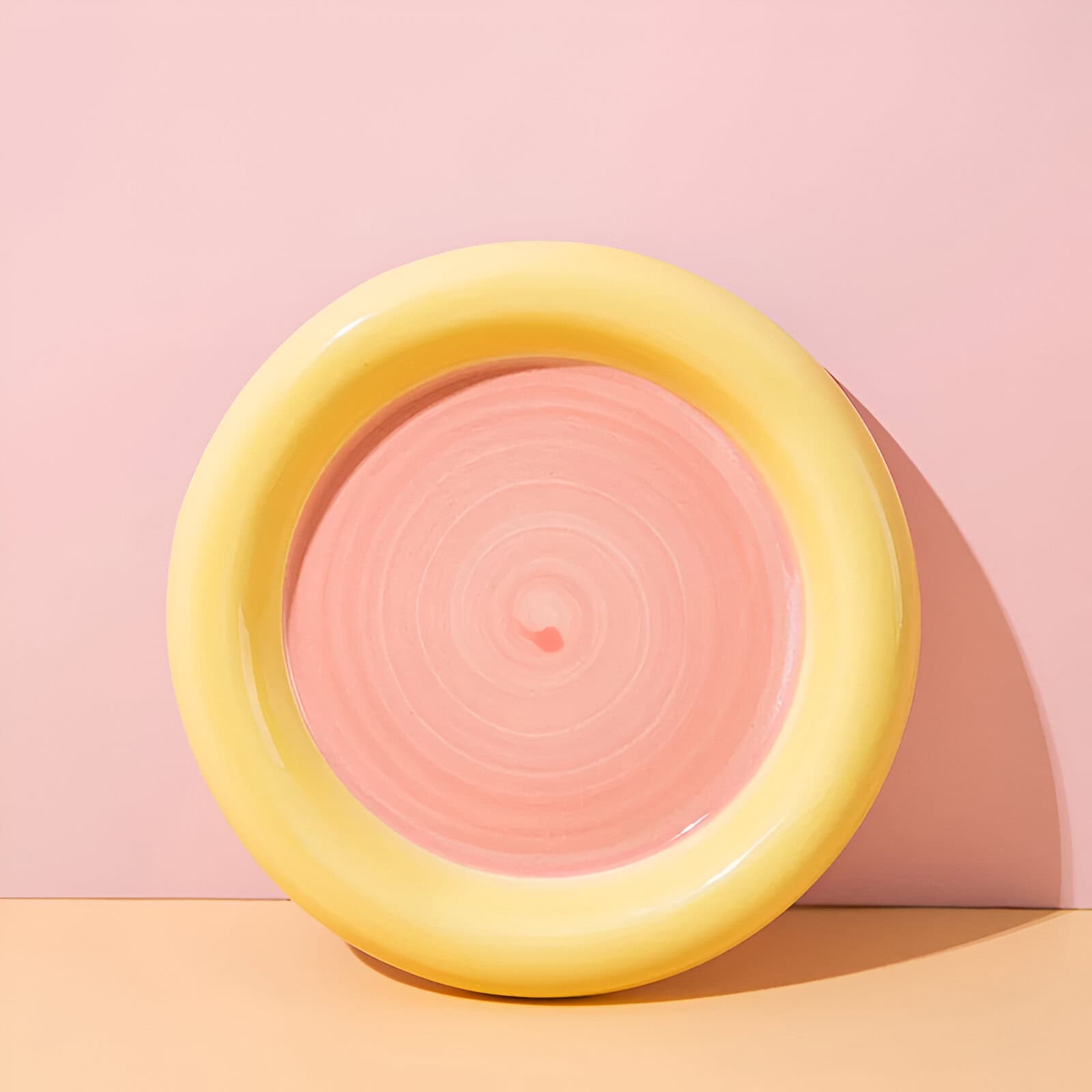 Vibrant pink and yellow abstract ceramic bowl with concentric circular design, displayed on a pastel pink and peach background, emphasizing modern and colorful home decor.
