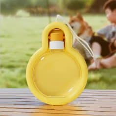 Bright yellow floatation device for dogs on a wooden surface with outdoor park background and a child playing with a dog, emphasizing pet safety during water activities.