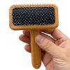 Pink hairbrush with black cushion and white bristles for scalp massage and hair detangling. Hand-held wooden hairbrush ideal for everyday grooming and hair care routines.