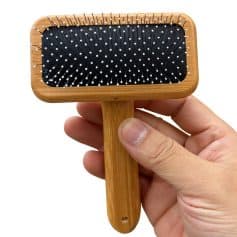 Pink hairbrush with black cushion and white bristles for scalp massage and hair detangling. Hand-held wooden hairbrush ideal for everyday grooming and hair care routines.