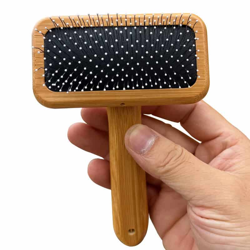 Pink hairbrush with black cushion and white bristles for scalp massage and hair detangling. Hand-held wooden hairbrush ideal for everyday grooming and hair care routines.