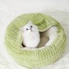 Fluffy white kitten sitting inside a cozy, round green pet bed, perfect for cats and small animals, with soft plush texture providing comfort and warmth.