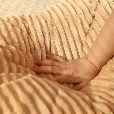 Silky beige textured fabric with a hand resting on it, luxurious material, plush and soft, possibly sleepwear or home decor, warm tone, detailed close-up image for fashion or interior design SEO.